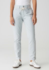 Pantalons en coton bleu clair, effilés, avec une taille à cordon de serrage, poches avant, et assortis à des baskets blanches. Texture lisse et coupe décontractée.