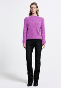 Fioletowy sweter dziany z okrągłym dekoltem i długimi rękawami, zestawiony z czarnymi dzwonowymi dżinsami. Sweter posiada teksturowaną strukturę materiału.