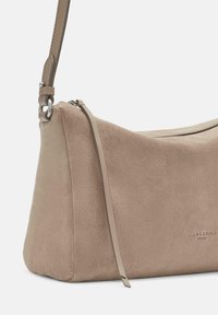 Borsa a spalla in suede beige con dettagli in pelle liscia, forma curvata e chiusura con zip. Include una tracolla rimovibile.