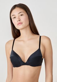 Sujeción negra con aros que presenta copas suaves y acolchadas con un diseño de escote pronunciado. Tirantes delgados ajustables y un acabado sin costuras.