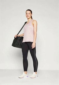 Svart treningsbag, lyse rosa tanktop, svarte leggings med hvite sidestriper, og hvite joggesko med lilla akenter.