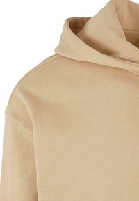 Hoodie beige realizzato in un tessuto morbido e leggero, con una vestibilità comoda e un cappuccio con coulisse. Texture liscia con dettagli a costine.