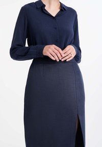 Námořnická modrá košile na knoflíky s límečkem a dlouhými rukávy, spárovaná s tužkovou sukní vysokého pasu s bočním rozparkem a texturovanou tkaninou.