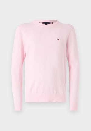 Světle růžový pletený svetr s dlouhými rukávy, kulatým výstřihem a malou nápisovou nášivkou na hrudi. Materiál vypadá měkký a má hladkou strukturu.