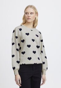 Maglione grigio realizzato in tessuto morbido, con motivi a cuore blu navy sparsi su tutta la superficie. Collo a giro e maniche lunghe leggermente a sbuffo.