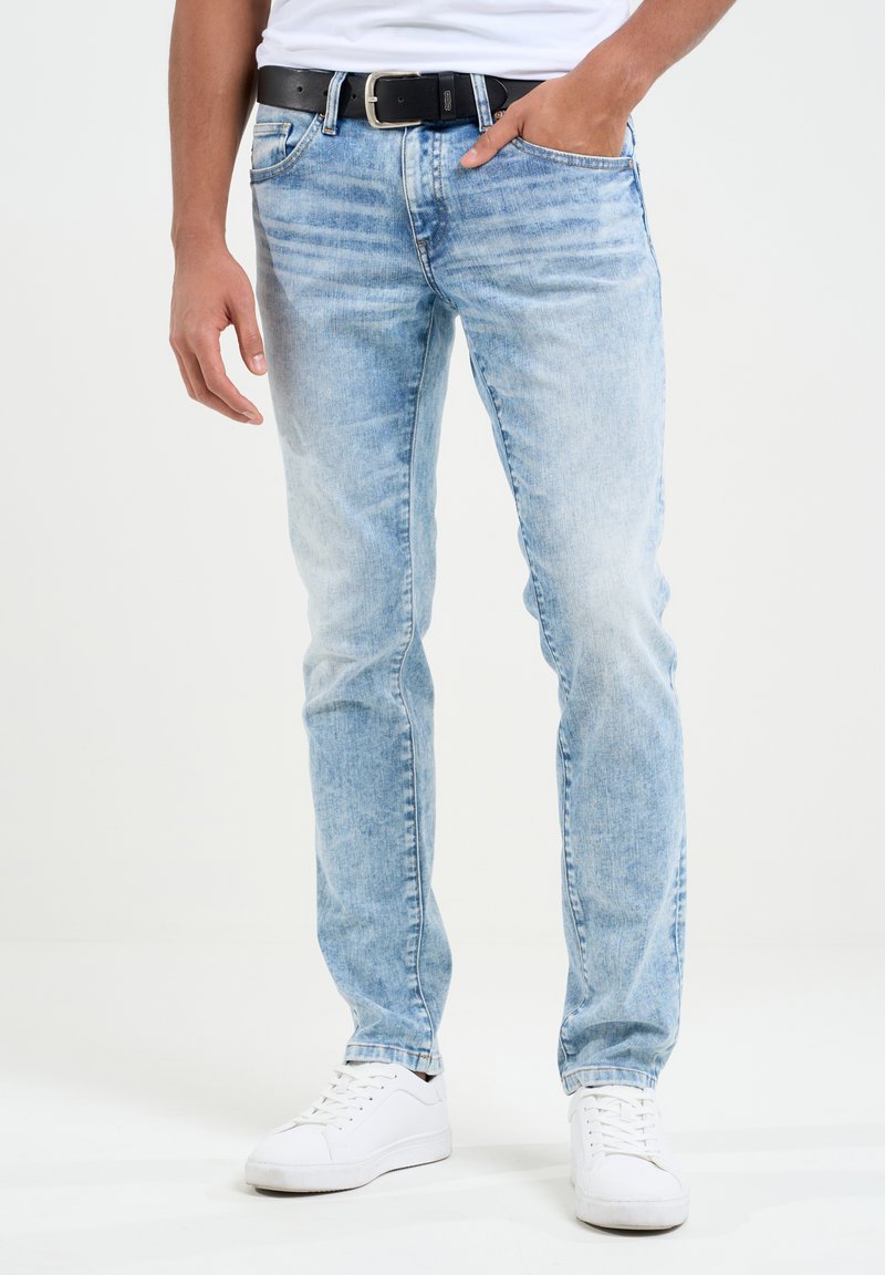 Šviesiai mėlyni džinsai su tiesiais džinsais, išblukusiu plovimu, penkių kišenių dizainu ir juodu diržu. Derinami su baltomis sportinėmis bateliais.