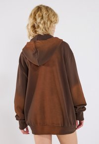 Oversized brown hoodie with a gradient effect, featuring a kangaroo pocket, ribbed cuffs, and a drawstring hood. Soft texture.