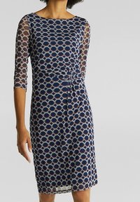 Marinblå klänning med genomskinliga ärmar, med ett cirkulärt mönster i ljusa färger. Figursydd midja, knälängd, med en snodd detalj framtill.