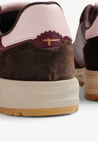 Brown suede and burgundy leather sneakers feature a pink accent on the heel, gold logo detail, and a textured cream and gum sole.