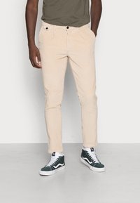 Béžové manšestrové kalhoty slim fit s předními kapsami a zapínáním na knoflík, doplněné o zelené vysoké tenisky a tmavě olivové tričko.