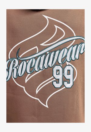 Hnedá látka s odvážnym bielym a tyrkysovým vyšitým textom "Rocawear" a číslom "99," s dekoratívnym vzorom pripomínajúcim plameň.