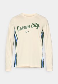 Dlhý rukáv krémového športového trička s nápisom „Cream City“ v zelenej farbe, so zeleno-modrými pruhmi na bokoch a logom Nike.