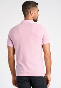 Camisa de polo rosa de manga corta, con acentos blancos en el cuello y las mangas. La tela parece suave con un ligero brillo.