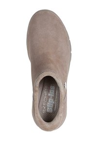 Zapato slip-on de ante beige con puntera redondeada, interior texturizado y un sutil patrón de logo en la plantilla. Diseño suave y acolchado.