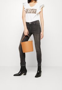 Camiseta blanca con mangas con volantes y un gráfico de estampado de leopardo, combinada con jeans pitillo gris oscuro y botines negros, sosteniendo un bolso tipo cubo color marrón claro.