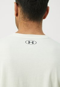 Lichtgrijs T-shirt met een ronde hals, voorzien van een zwart Under Armour-logo op de bovenrug, fijne textuur, ontspannen pasvorm.