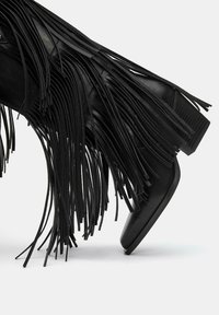 Črne usnjene gležnjarje z dolgimi resicami, s stožčastim peto in gladko teksturo, ki imajo obliko koničastega prsta.