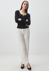 Top nero a maniche lunghe con scollatura quadrata, abbinato a pantaloni bianchi a gamba dritta e scarpe nere con tacco alto. Design minimalista.