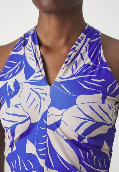  Haut à col halter présentant un motif de feuilles bleu et crème sur un tissu doux. Le design en V améliore l'apparence générale avec une texture lisse.