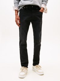 Zwarte denim jeans hebben een slim fit ontwerp met vijf zakken, metalen hardware en een subtiele logo-detail. Gestyled met witte sneakers.