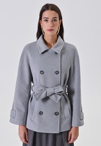 Cappotto grigio a doppio petto con cintura legata, ampio colletto e due grandi bottoni; realizzato in tessuto testurizzato con tasche laterali e maniche lunghe.