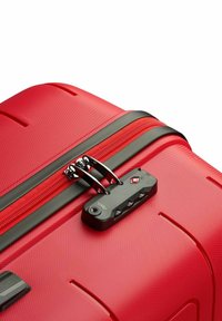 Maleta rígida roja con superficie texturizada, detalles de cremallera negra y un candado aprobado por la TSA con combinación numérica.