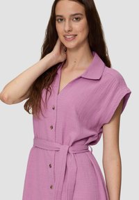 Liliowa sukienka z guzikami, wykonana z teksturowanej tkaniny, z krótkimi rękawami, paskiem w talii i brązowymi guzikami jako akcentami.