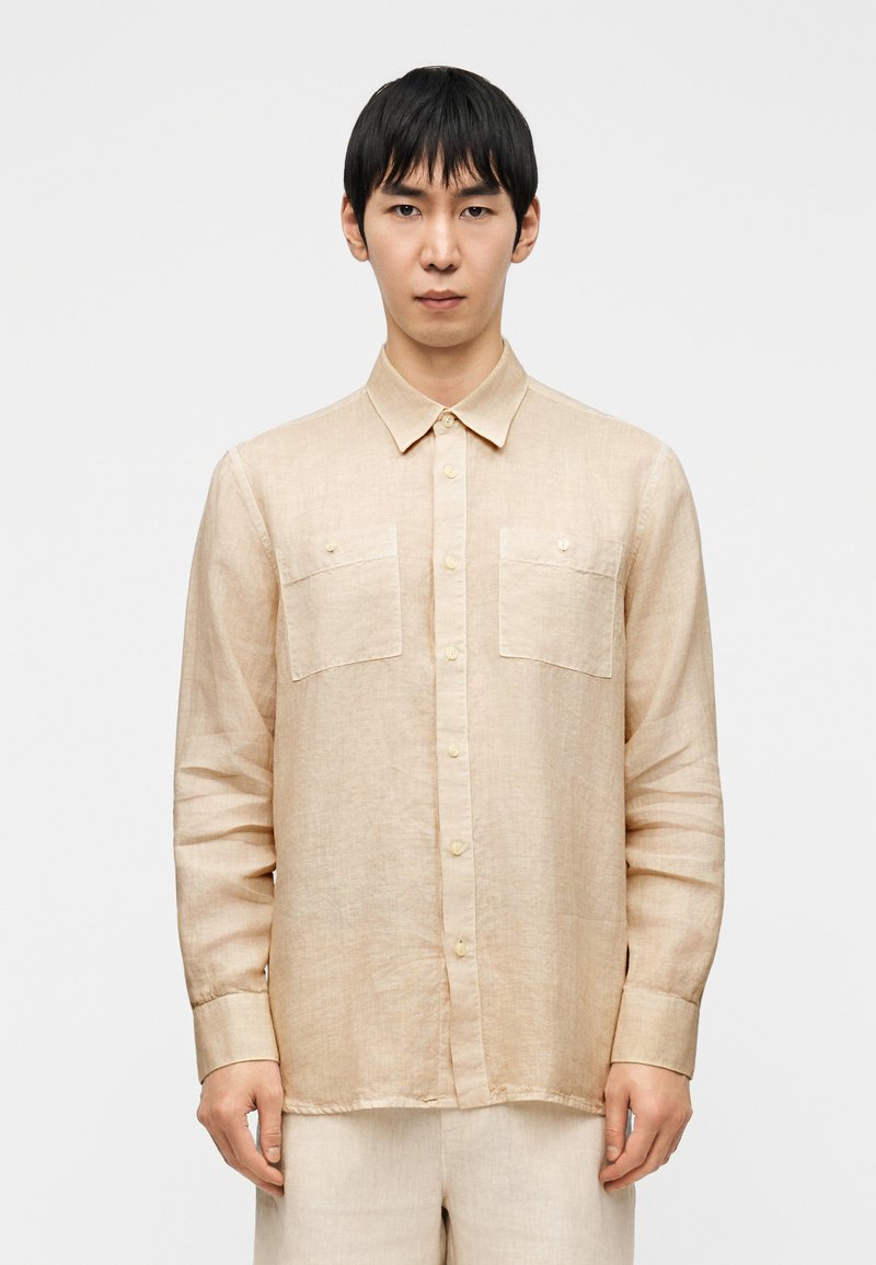 Μπεζ μακρυμάνικο πουκάμισο από ελαφρύ λινό μείγμα, με δύο τσέπες στο στήθος, γιακά με κουμπιά και λεπτή υφή.