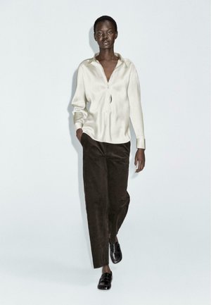 White silk shirt with a pointed collar, paired with dark brown wide-leg corduroy trousers and black slip-on shoes. Simple and contemporary design.