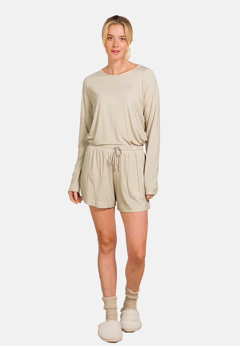 Helles beiges Loungewear-Set bestehend aus einem langärmeligen Oberteil mit einem dezenten Muster und Shorts mit Kordelzug. Kombiniert mit cremefarbenen, flauschigen Socken.
