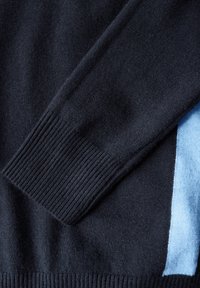 Marineblaue Strickjacke mit einem hellblauen vertikalen Paneel, gerippten Bündchen und glatter Textur. Fokus auf dem Design von Ärmeln und Schultern.