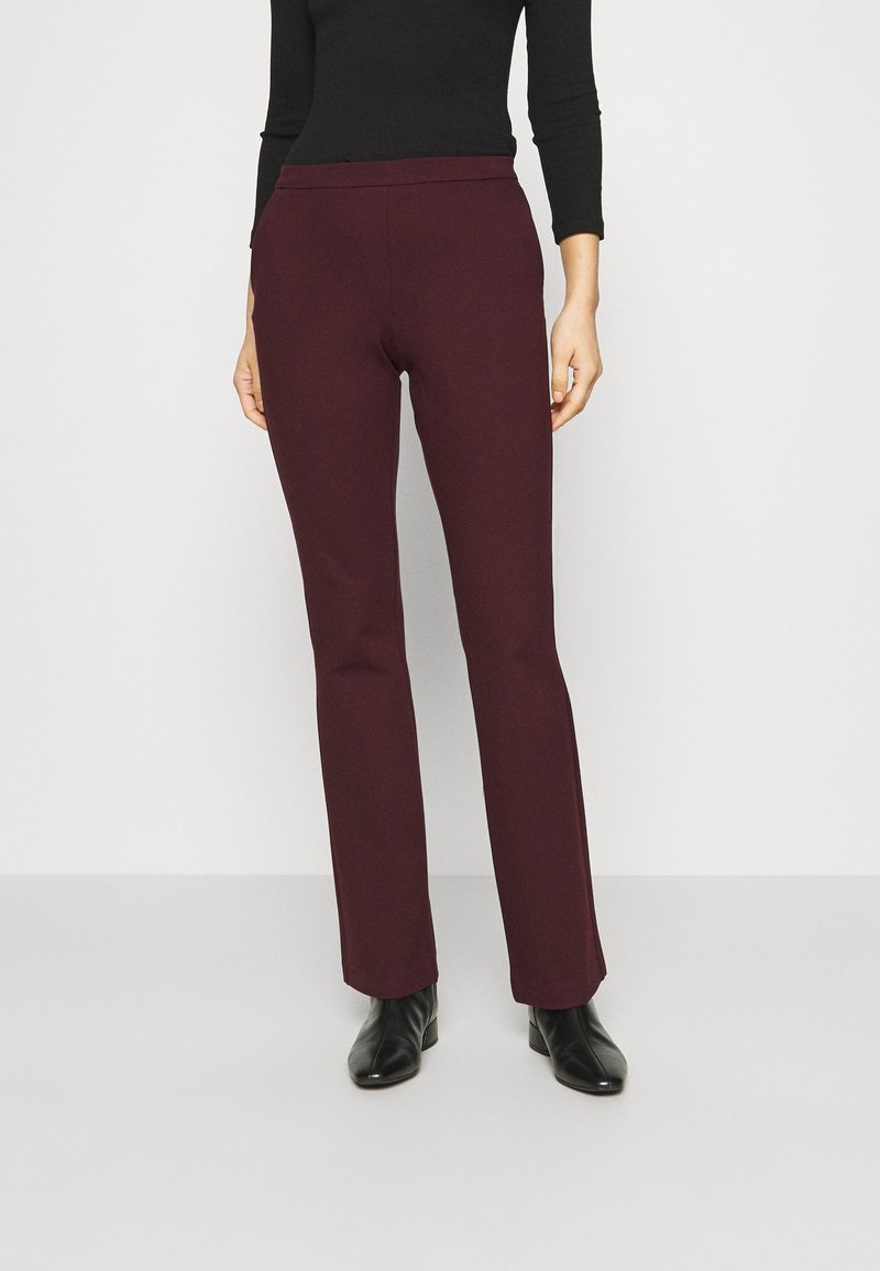 Pantalons slim-fit bordeaux en tissu doux, dotés d'une taille confortable et de jambes droites, associés à des bottines noires.