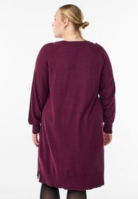 Haljina s dugim rukavima do koljena u tamno bordo boji. Mekani pleteni materijal s bočnim prorezima. Udoban kroj s zaobljenim izrezom na vratu.