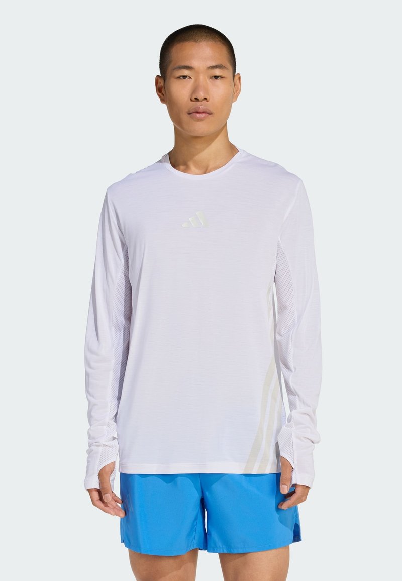 Langærmet hvid sportstrøje med mesh-paneler, der har et diskret logo på brystet og tommelhuller, kombineret med blå shorts.