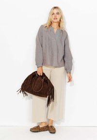 Blouse rayée à manches longues avec un col en V, pantalon beige à jambe large, sac en suède marron avec franges et chaussures à enfiler imprimé léopard.