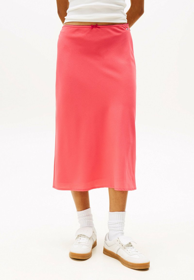 Lang, lyserød nederdel lavet af blødt, strækbart stof med snor i taljen. Kombineret med hvide sneakers og sokker. Designet til afslappet brug.