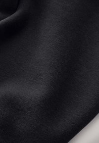 Tessuto di cotone nero con una trama liscia, che mostra un raffinato motivo a maglia e un leggero splendore. Il materiale appare leggero e flessibile.