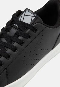 Baskets en cuir noir avec lacets noirs, panneau latéral perforé, semelle blanche et étiquette "COURT LINE" sur la languette.