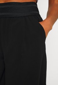 Schwarze Hose mit einem breiten, strukturierten Bund und einer Seitentasche, aus glattem Stoff und mit einer entspannten Passform.