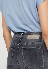 Vaqueros de denim gris ajustados con una textura descolorida y costuras visibles, que presentan una etiqueta con "WON HUNDRED" en la cinturilla trasera.