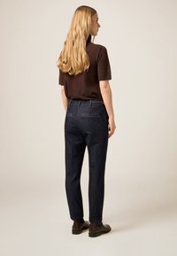 Pantalones de mezclilla azul oscuro con un corte entallado, complementados con un suéter marrón de punto. Líneas limpias y puños doblados ofrecen una silueta moderna.