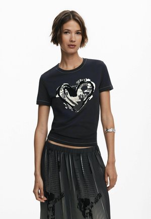Navy cotton t-shirt with a silver heart graphic, short sleeves, and contrasting stitching, paired with a pleated black skirt.