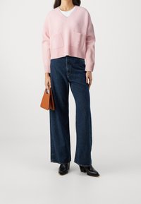 Hellrosa gerippter, kurz geschnittener Pullover mit zwei vorderen Taschen, kombiniert mit hoch taillierter, dunkelblauer Jeans mit weitem Bein und schwarzen, hochhackigen Stiefeletten.