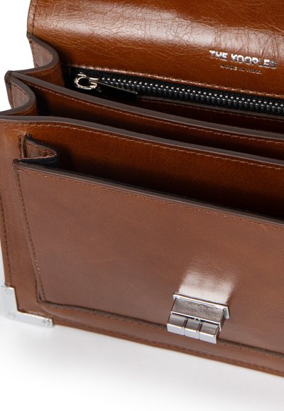 Borsa a mano in pelle marrone con una texture liscia, dotata di scomparti multipli, una cerniera argentata e un dettaglio a chiusura metallica.