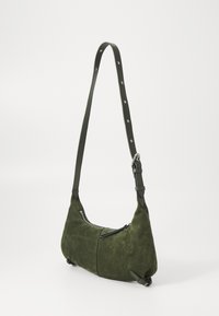 Grønn semsket skulderveske med en buet form, justerbar reim med sølvnipper, og sidelomme med glidelås for lukking.