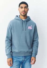 Šviesiai mėlynas džemperis su raišteliu apjuostu gobtuvu, ribotais rankogaliais ir apačia, ant kairiojo krūtinės šono yra rožinis "Pink Floyd" logotipas.