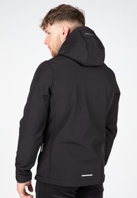 Veste softshell noire avec capuche ; design ajusté, texture lisse et accents réfléchissants à l'arrière. Comprend des coutures latérales et de bras.