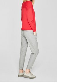 Pull en maille rouge avec un empiècement texturé, associé à un pantalon gris clair fuselé avec des revers roulés et des baskets gris clair.