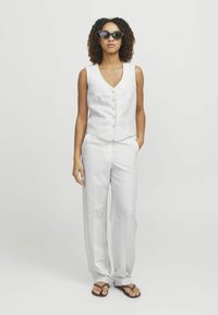 Biały, dopasowany kamizelka z dekoltem w serek i pięcioma guzikami, w połączeniu z szerokimi białymi spodniami. Noszona z czarnymi okularami w kocim kształcie i klapkami.