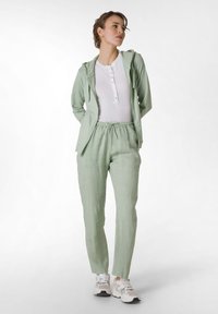 Sudadera verde clara con cordones, camisa blanca de botones y pantalones verdes claros, combinados con zapatillas blancas. Tela suave y corte relajado.